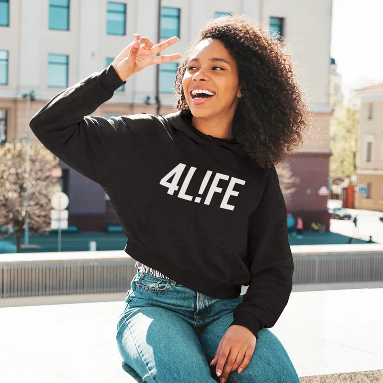 Woman with curly hair making a peace sign, wearing a black cropped hoodie with white 4L!FE artwork in an outdoor lifestyle mockup